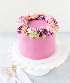 a pink cake decorated with flowers on a white platter next to a fork and napkin