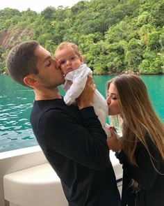 a man holding a baby while standing next to a woman on a boat in the water