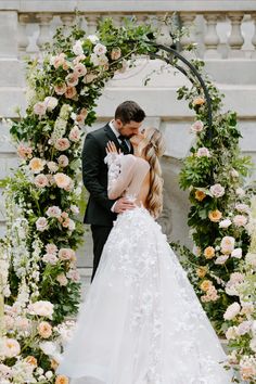 a bride and groom kissing in front of a floral arch