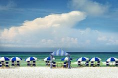 blue and white striped umbrellas on the beach with chairs under them in front of the ocean