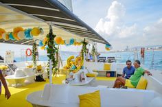 two people sitting on the back of a boat with yellow and white decorations hanging from it