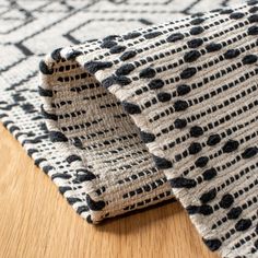 a close up of a rug on a wooden floor with a black and white pattern