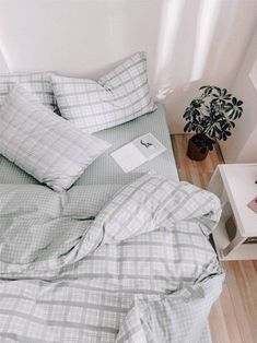 a bed with plaid sheets and pillows next to a small potted plant on the side table