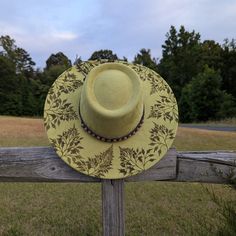 This hand burnt faux suede wide brim boater hat makes a perfect addition to any nature lovers wardrobe. The earthen chartreuse green material burns a gorgeous deep green allowing the design to stand out. Whimsical ferns, that appear to be blowing in the breeze, are intricately burned by hand using a pyrography machine around the entire crown of the hat. The design is original and completely freehanded. For a finishing touch the hat is adorned with a wooden beaded tie-back hat band. Hat Materials: Polyester Hat is 56cm-58cm, but fits most with an adjustable tie band inside Hat has a roughly 10 CM brim. Colors may vary slightly from screen to screen Bohemian Boater Hat With Curved Brim For Garden Party, Bohemian Boater Hat For Garden Party With Curved Brim, Bohemian Boater Hat With Flat Brim For Garden Party, Bohemian Boater Hat With Short Brim For Garden Party, Bohemian Boater Hat For Garden Party With Short Brim, Bohemian Boater Hat For Kentucky Derby With Flat Brim, Bohemian Boater Hat For Kentucky Derby, Bohemian Boater Hat For Garden Party, Bohemian Boater Hat For Kentucky Derby And Country Events