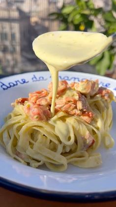 a spoon is pouring sauce over some pasta on a white plate with blue rims