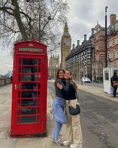 two women hugging each other in front of a red phone booth on the street with big ben in the background