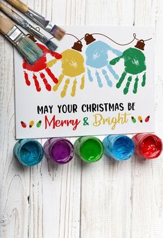 a christmas card with paint and crayons next to it on a white wooden surface