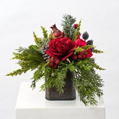 a bouquet of red flowers and greenery in a square vase on a white surface