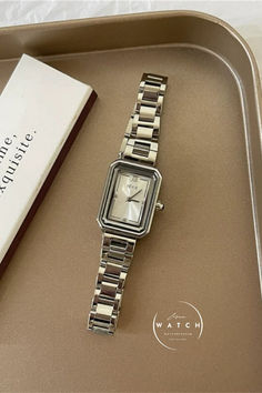 This sophisticated watch features a small rectangular white dial, framed in gold and silver, with a sleek stainless steel strap available in gold, silver, and rose gold. Its comfortable and versatile design complements any style, making it a favorite among women. Trendy Rectangular Quartz Watch, Silver Watch With Rectangular Dial For Everyday, Silver Rectangular Metal Watch, Rectangular Silver Metal Watch, Modern Rectangular Metal Watches, Golden Bracelet, Square Face, Square Faces, Timeless Accessories