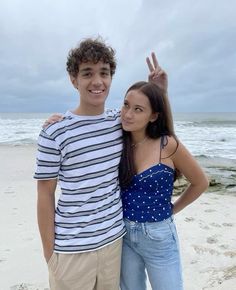 a man and woman standing on top of a sandy beach next to the ocean with their hands in the air