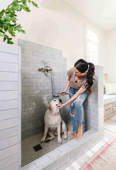 a woman is petting a dog in the shower while another sits on the floor