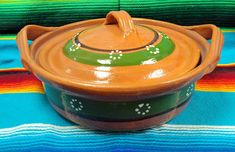 a brown and green pot sitting on top of a colorful table cloth