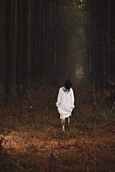 a woman walking through a forest in the dark with her back turned to the camera