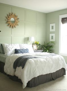 a bedroom with green walls, white bedding and a sun shaped mirror on the wall