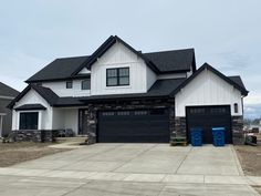 a large house with two blue trash cans in front of the garage door and windows