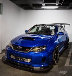 a blue subarunt is parked in a parking garage next to a white wall