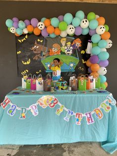 a birthday party with balloons and decorations on a table in front of a blackboard