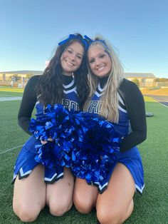 two cheerleaders sitting on the ground with their pom poms