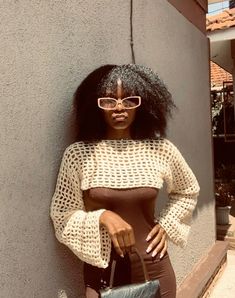 a woman wearing glasses leaning against a wall with her hand on her hip and looking at the camera