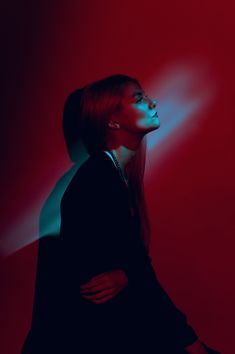 a woman with long hair standing in front of a red and blue background, looking up