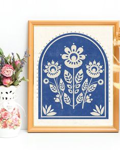 a blue and white framed artwork next to a vase with flowers