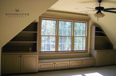 an attic bedroom with built - in bookshelves, ceiling fan and large window