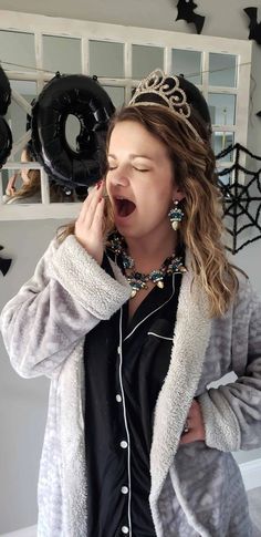 a woman with her mouth open wearing a tiara and singing in front of black balloons