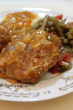 some meat and vegetables on a plate with gravy over the top is sitting on a table