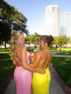 two beautiful women standing next to each other on a brick walkway in front of tall buildings