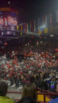 a large group of people in graduation gowns and with red and white balloons are gathered at the front of an auditorium