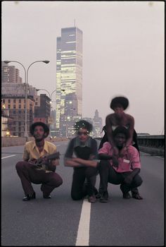 three men sitting on the side of a road in front of a cityscape