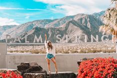 a woman standing in front of palm springs sign with her arms up and hands raised