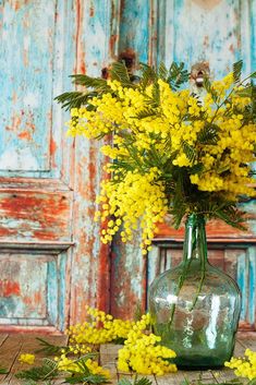 yellow flowers in a green glass vase on a wooden table next to an old door