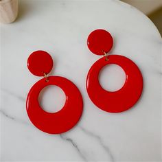 Stylish Red Dangle Hoops with a Modern Twist. Red hoop earrings in a retro style are always in vogue, having remained popular across several decades, from the 50's, 60's, 70's, 80's, and beyond. Handmade with care, these earrings are not only trendy but also enjoyable and fun to wear. Treat yourself or surprise a friend with a gift of these vibrant, medium-sized hoops made from polymer clay and coated with resin on both sides. Featuring an open circular orange hoop at the bottom connected to mat Red Clip-on Earrings For Party, Red Clip-on Round Jewelry, Red Round Clip-on Jewelry, Trendy Red Circular Jewelry, Retro Red Dangle Earrings, Retro Small Hoop Earrings For Gifts, Red Pierced Hoop Earrings, Modern Red Hoop Earrings, Modern Red Round Earrings