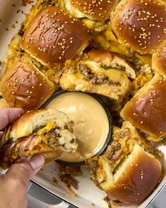 a person dipping sauce on top of sliders in a casserole dish with bread