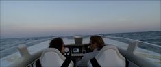 two people sitting in the back of a boat looking out over the ocean at sunset