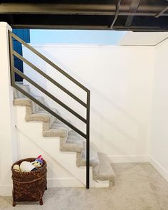 a basket sitting on the floor next to a stair case in a room with white walls