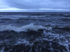 the ocean is very choppy and dark with some clouds in the sky above it