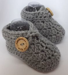 a pair of gray crocheted slippers with a wooden button