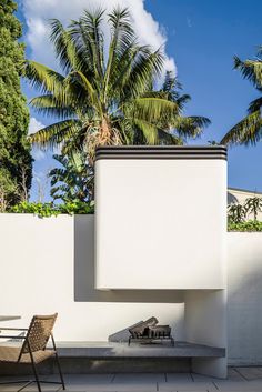 an outdoor table and chair are next to a white wall with palm trees in the background