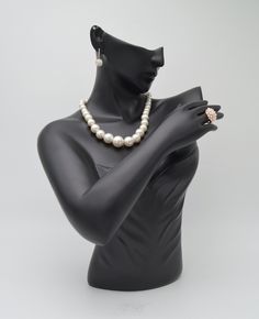 a mannequin with a necklace and ring on it's arm, in front of a white background