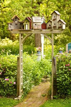 a garden with lots of bird houses on top of the wooden structure in front of flowers and trees