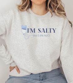 "This humorous and funny sweatshirt is a great one to wear to work as an IV infusion nurse, PICC line nurse, Med/Surg, ICU, ER or any healthcare worker that works with IV fluid. This sweatshirt is sure to give you or someone you know a laugh and would be a great gift.  This unisex heavy blend crewneck is made of polyester and cotton to provide a comfortable and cozy feel. The collar is ribbed knit and retains its shape after every wash.  WHAT IT SAYS: I'm Salty like 0.9% NaCl ITEM DETAILS:  -50% cotton, 50% polyester -Medium-heavy fabric  -Loose fit -Sewn-in label -Runs true to size, BUT if you're looking for a more \"baggy\" fit we suggest sizing up! **PLEASE NOTE! The print size/proportion may be slightly off on mock-up images; for the most accurate proportions of the print size please r Med Surg Nurse Shirt, Funny Er Nurse Shirts, Nurse Quotes Funny Humor, Cotton Relaxed Fit Nursing Sweatshirt, Cotton Nursing-friendly Relaxed Fit Sweatshirt, Nursing Cotton Sweatshirt With Crew Neck, Casual Cotton Sweatshirt For Nursing, Er Nurse Shirt, Nurse Sweatshirt Ideas