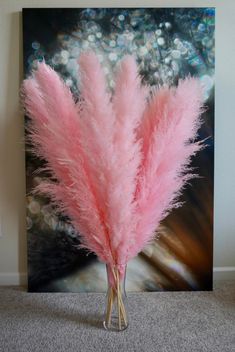 a vase filled with pink feathers sitting on top of a carpeted floor next to a painting