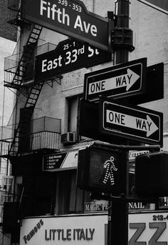 black and white photograph of street signs in front of a brick building on fifth avenue