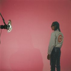 a man standing in front of a pink wall with a camera attached to his shoulder