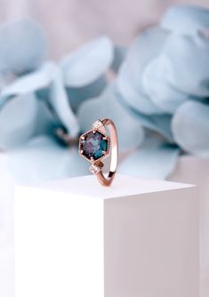 a blue diamond ring sitting on top of a white block with flowers in the background