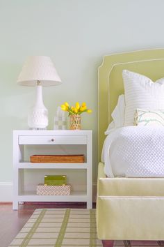 a white bed sitting next to a lamp on top of a wooden table in a bedroom