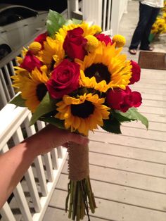 a bouquet of sunflowers and roses is held by a person on a porch