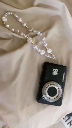 a black camera sitting on top of a bed next to a pearl necklace